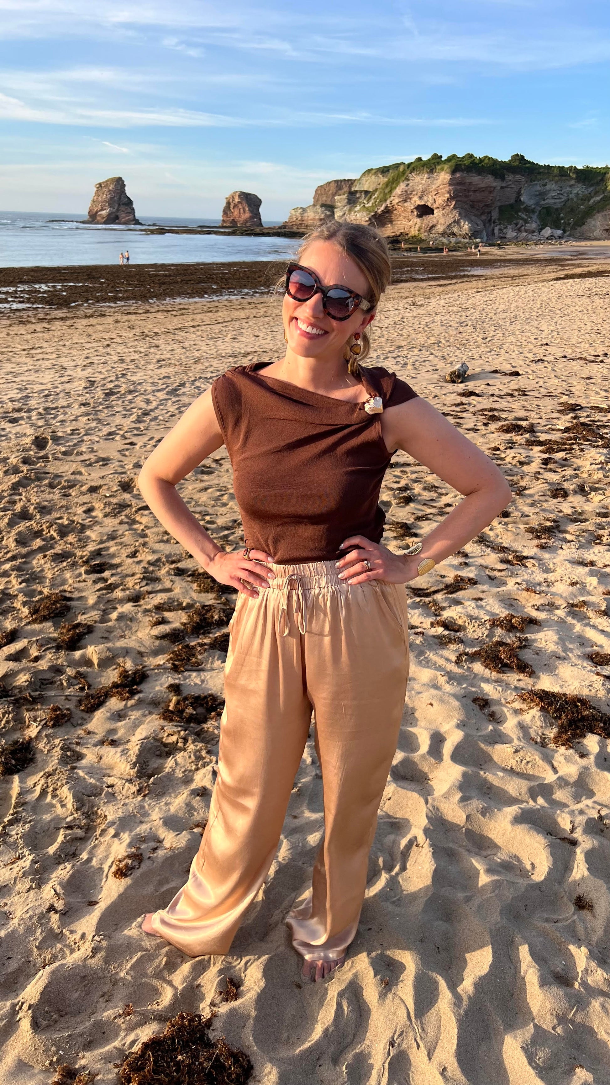 Top marron chocolat Arlo à encolure drapée et détail doré, porté avec pantalon satiné doré Oro, silhouette complète en bord de mer - HAVANA PARIS