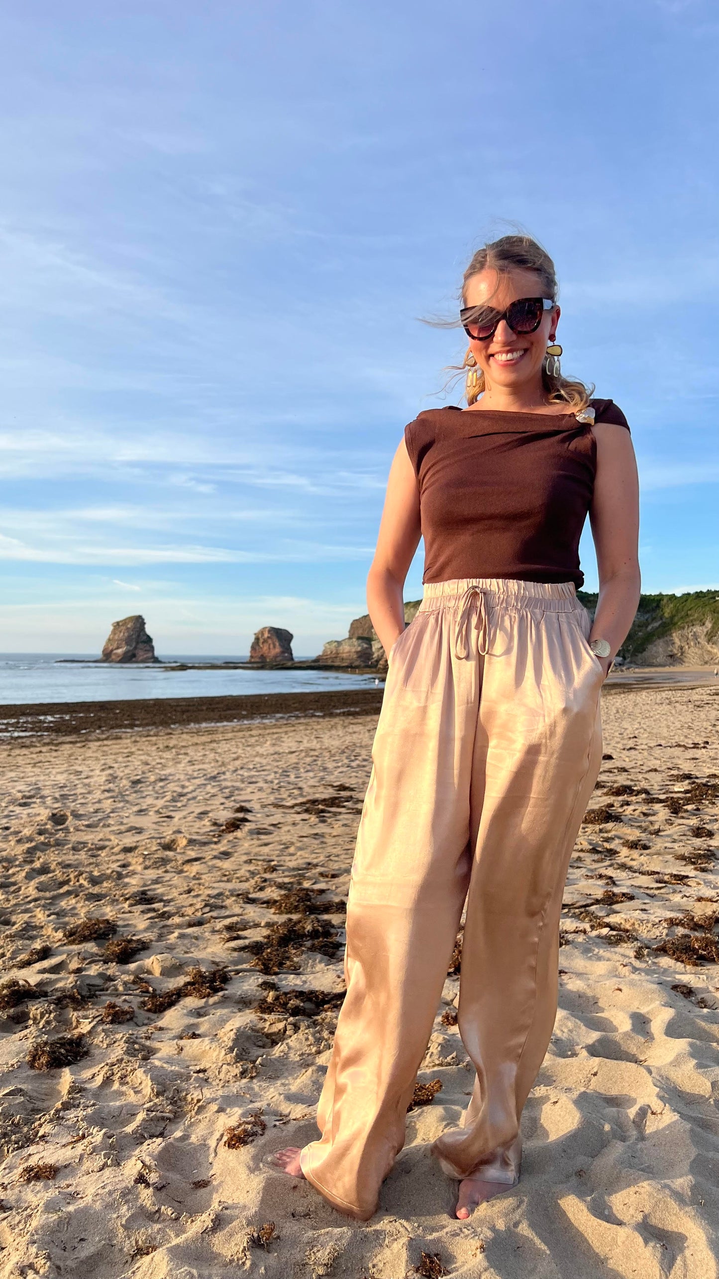 Pantalon satiné doré Oro fluide porté avec top marron, silhouette complète en bord de mer - HAVANA PARIS
