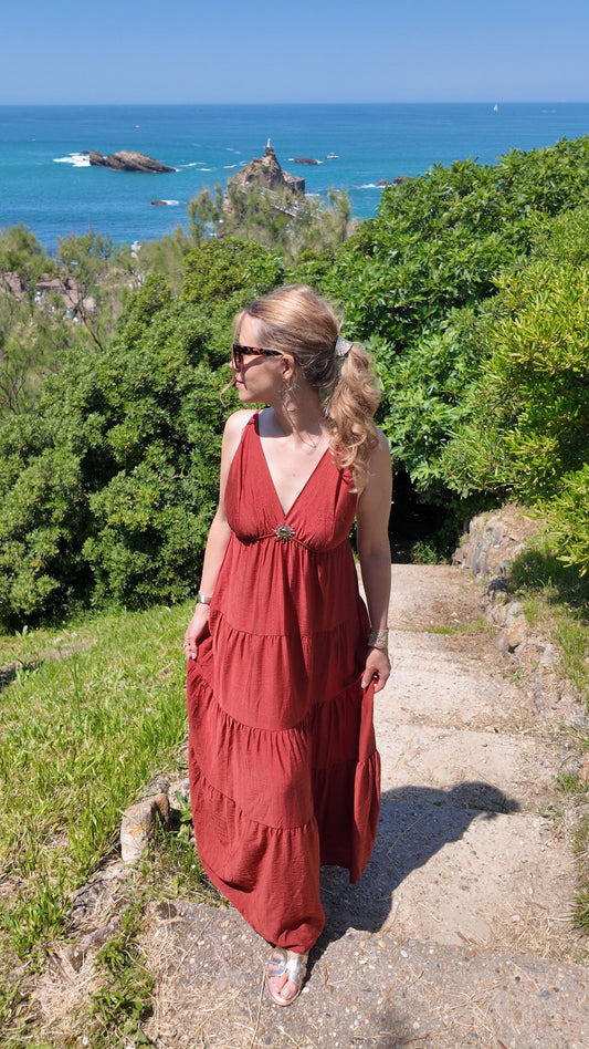 Robe longue terracotta Havane à coupe étagée et décolleté en V, broche soleil, portée en bord de mer - HAVANA PARIS